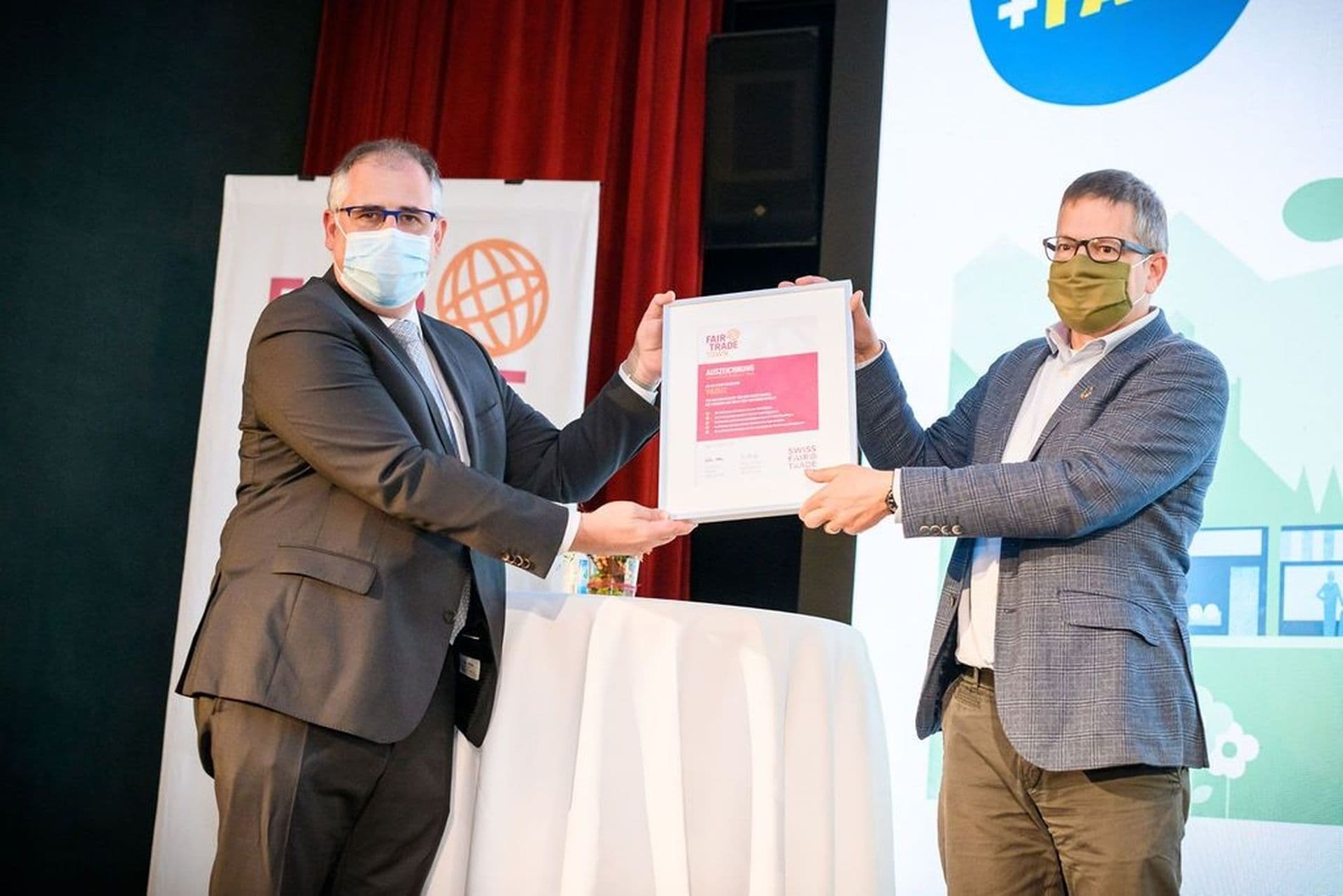 Ein Vertreter von Fair Trade Town überreicht Bürgermeister Manfred Bischof auf der Bühne im Rathaussaal eine gerahmte Urkunde. Damit wird Vaduz als erste Fair Trade Town Liechtensteins offiziell ausgezeichnet.
