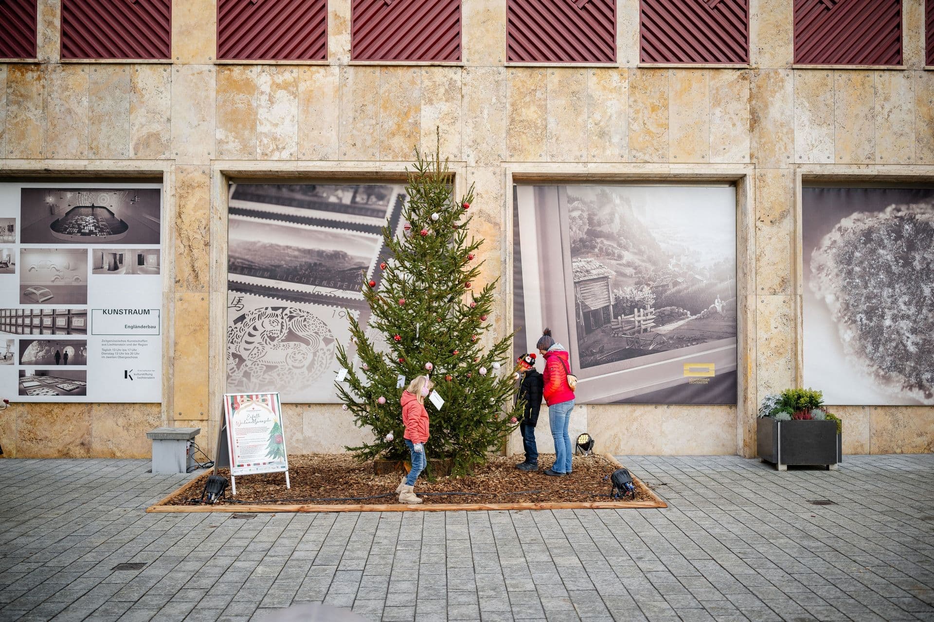 Drei Personen schauen sich den Wunschbaum im Weihnachtsstädtle 2024 an, der vor dem Landesmuseum steht. Das Bild symbolisiert die Weihnachtszeit.